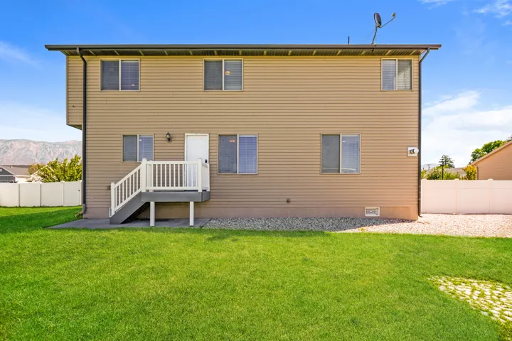 Two-story exterior with horizontal siding, white deck with stairs, ground-level green lawn, and gravel landscaping