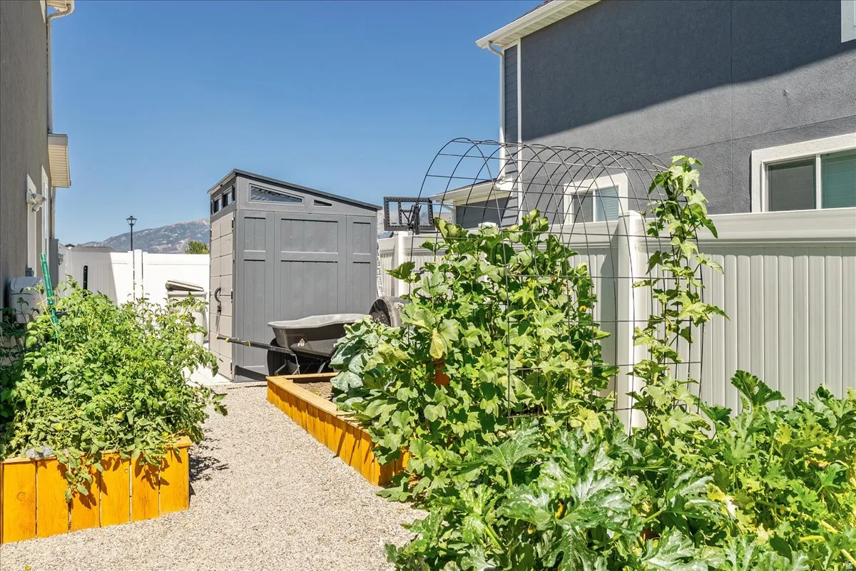 Gravel pathway bordered by raised garden beds, privacy fencing, and a storage shed