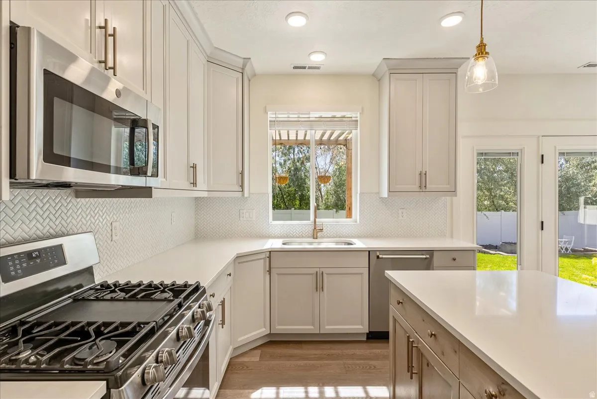 Kitchen featuring stainless steel appliances, white cabinetry, herringbone tile backsplash, light countertops, and wood-finish flooring