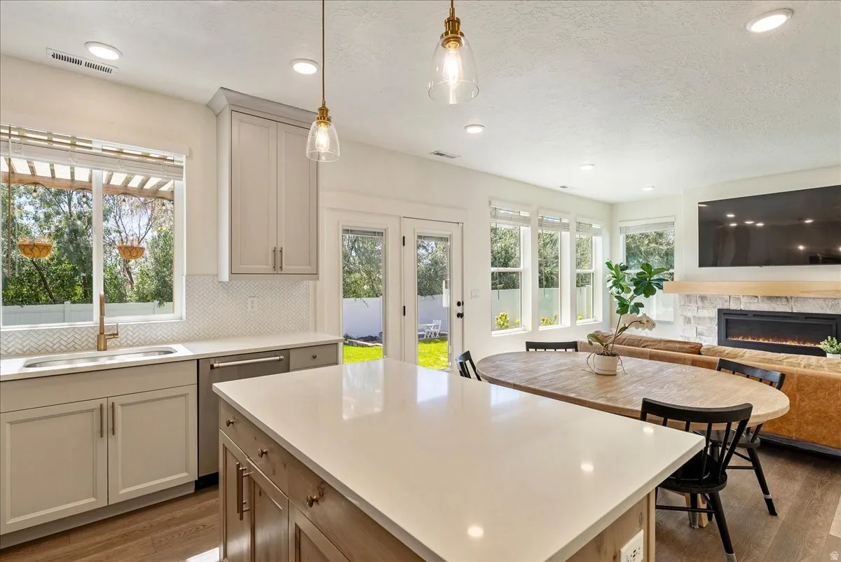Open-concept living space featuring a built-in electric fireplace, wood-finish flooring, a kitchen island with stone countertops, and ample natural light through multiple windows
