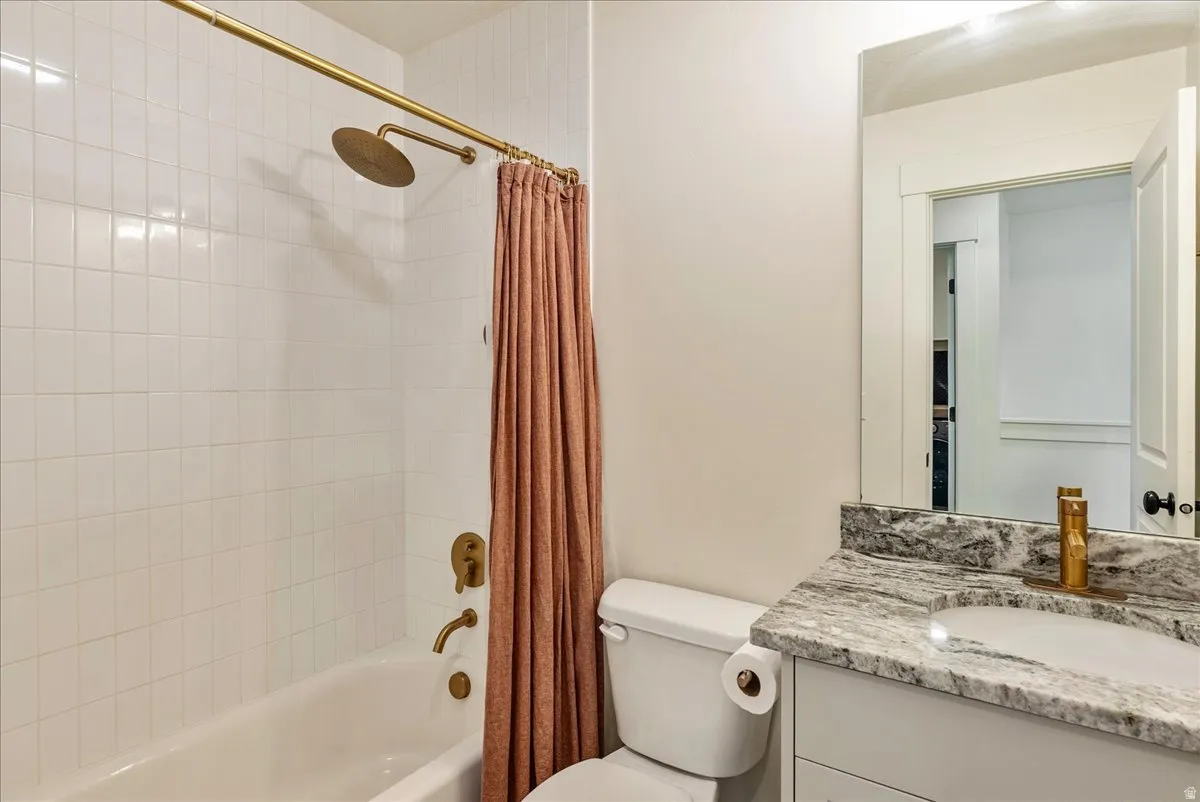 White subway tile shower surround with a rain shower head, bathtub with brass fixtures, vanity with a rectangular undermount sink, and a stone countertop