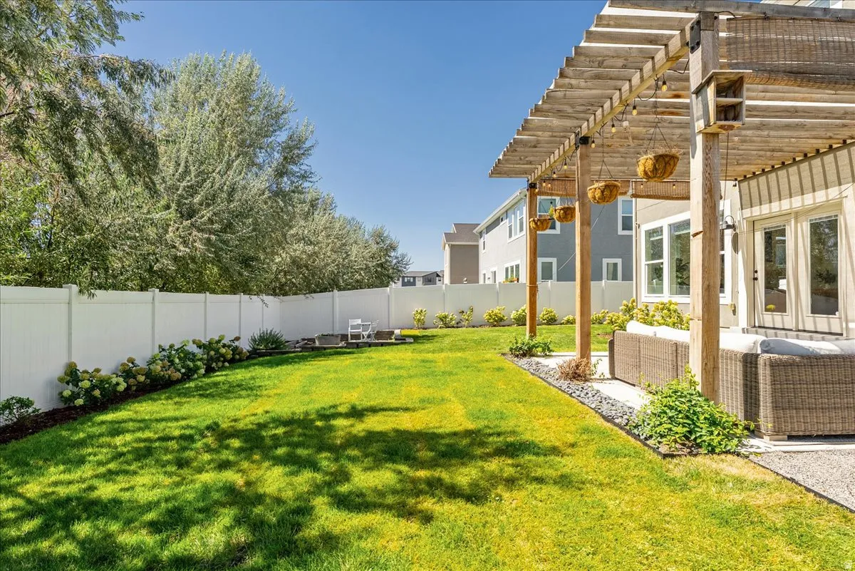 Expansive green lawn, white privacy fencing, natural wood pergola, concrete patio, and mature perimeter trees