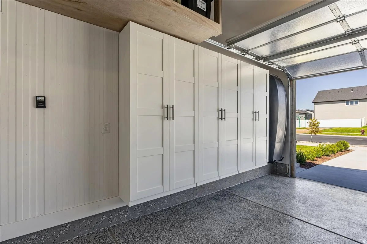 Garage featuring extensive built-in white cabinetry with black hardware, shiplap wall paneling, and a durable epoxy-coated concrete floor