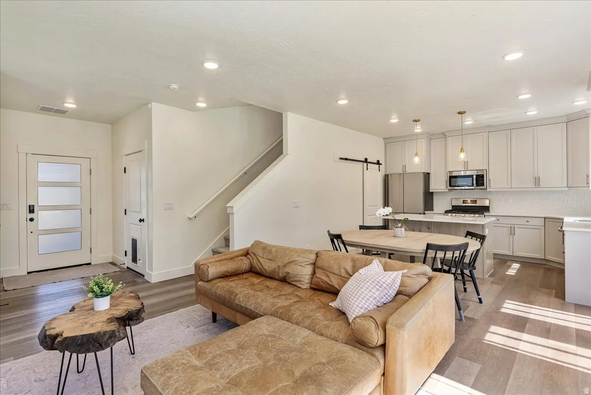 Open-concept living space featuring wood-finish flooring, recessed lighting, and a modern kitchen with stainless steel appliances, light cabinetry, and a subway tile backsplash