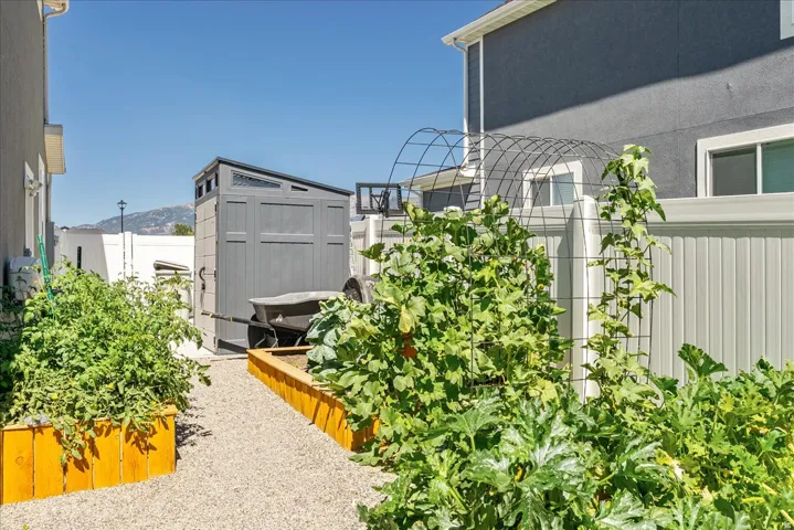 Gravel pathway bordered by raised garden beds, privacy fencing, and a storage shed
