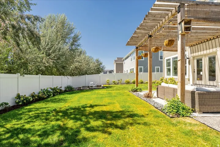 Expansive green lawn, white privacy fencing, natural wood pergola, concrete patio, and mature perimeter trees