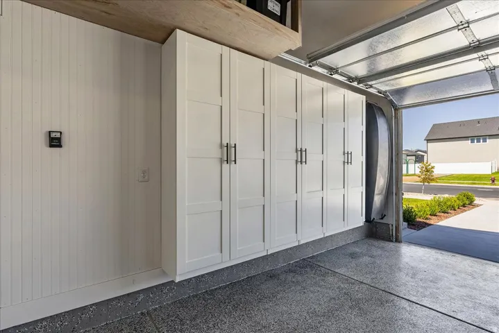 Garage featuring extensive built-in white cabinetry with black hardware, shiplap wall paneling, and a durable epoxy-coated concrete floor