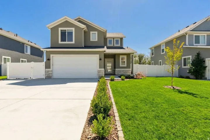 Contemporary stucco exterior with stone accents, a two-car garage, a concrete driveway, and a manicured lawn with established landscaping