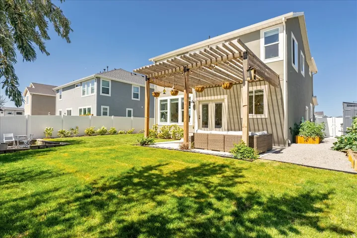 Expansive backyard featuring a manicured lawn, a large wood pergola, gravel pathway, and raised garden beds