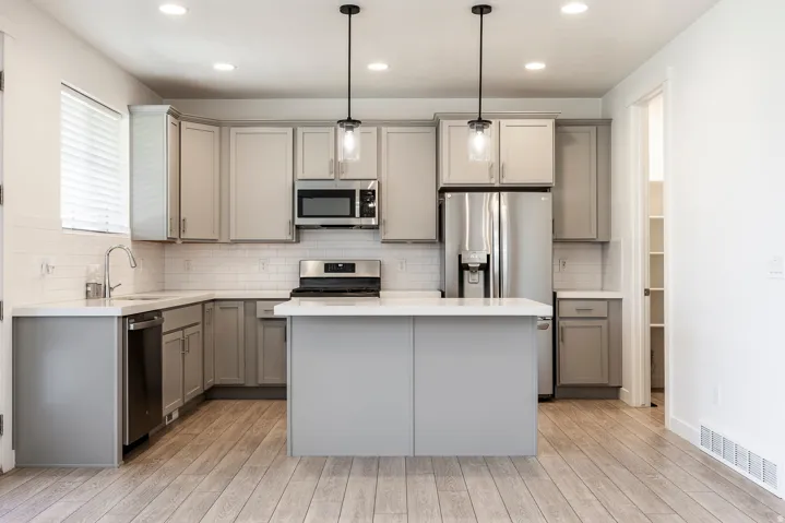 Modern kitchen featuring a central island, light wood-finish flooring, white subway tile backsplash, and stainless steel appliances