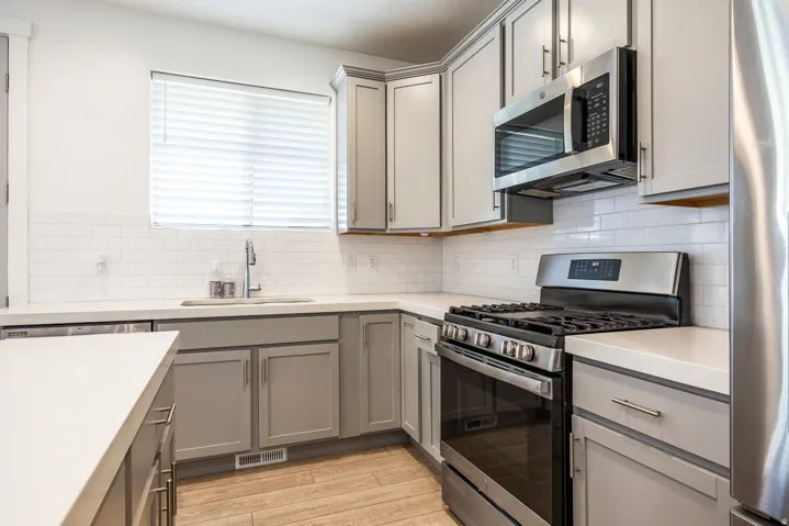 Kitchen featuring light grey cabinetry, white countertops, stainless steel appliances, white subway tile backsplash, and wood-finish flooring