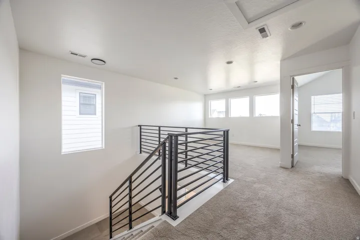 Carpeted upper-level space featuring a contemporary black metal railing and multiple windows