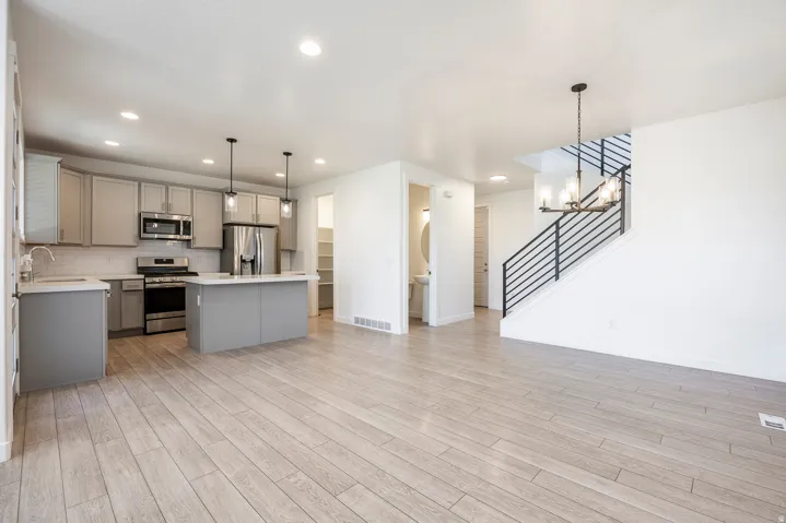 Open-concept living space with wood-finish flooring, a contemporary kitchen featuring stainless steel appliances and pendant lighting, a spacious island, and a modern staircase with metal railings