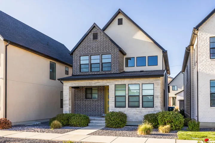 Contemporary exterior featuring contrasting brick and stucco finishes, black-framed windows, a covered front entry, and a gabled roofline