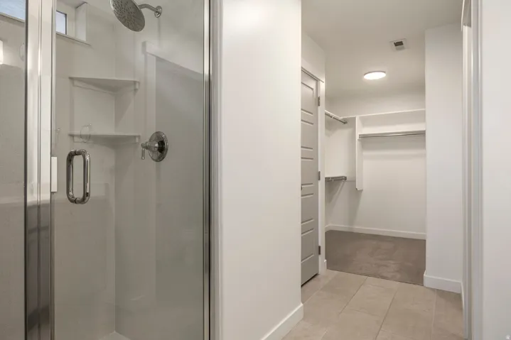 Walk-in shower with clear glass enclosure and corner shelving