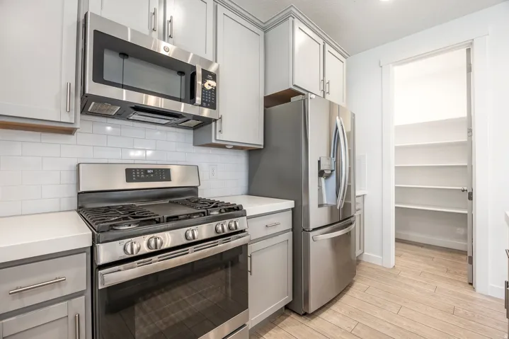 Modern kitchen featuring stainless steel gas range with six burners and convection oven, matching stainless steel refrigerator with French doors, white cabinetry with chrome hardware, subway tile backsplash, white quartz countertops, and wood-finish floor
