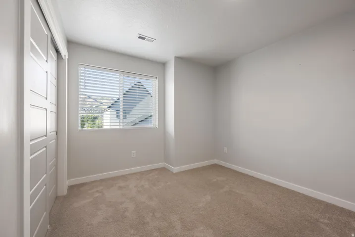 Carpeted flooring, neutral wall tones, window with blinds, and white bi-fold closet doors