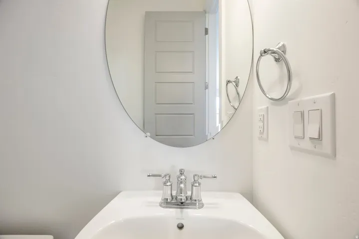 Pedestal sink with chrome faucet, oval wall mirror, and chrome towel ring