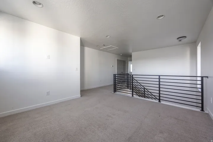Spacious upper-level room with neutral carpet flooring, white walls, and recessed ceiling lighting