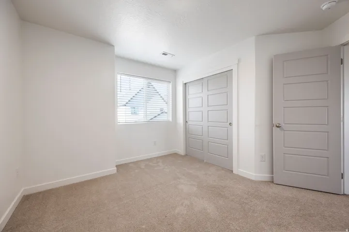 Neutral-toned carpeting, white walls, and a window with blinds provide a bright atmosphere