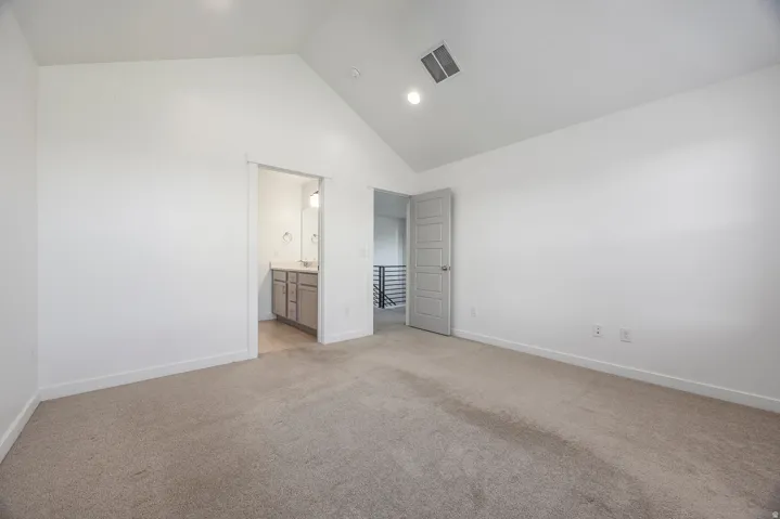 Vaulted ceiling, recessed lighting, carpet flooring, five-panel interior door, and an adjoining bathroom featuring a vanity with a rectangular sink