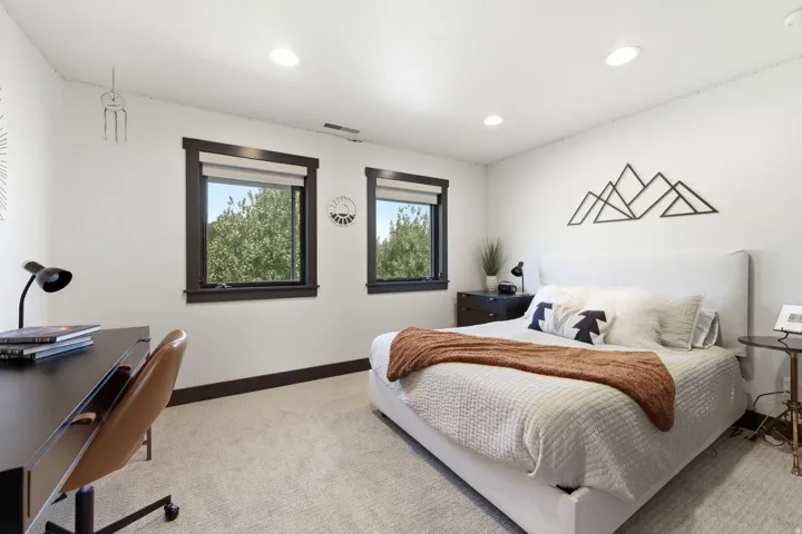 Recessed lighting illuminates the space, featuring two windows with dark trim and roller shades