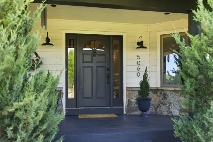 Welcoming front entry featuring a dark blue six-panel door with sidelights, flanked by dual black pendant fixtures and stone veneer accents