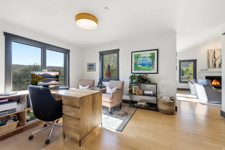 Bright interior space featuring light wood-finish flooring, multiple windows with dark trim, a built-in shelving unit, and a visible fireplace in the adjacent room