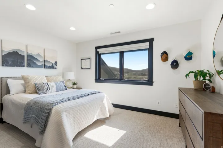 Recessed lighting, dark-trimmed window, upholstered headboard, light-colored carpeting, and light-colored walls