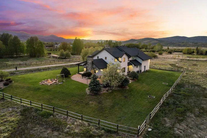 Expansive fenced yard featuring a stone fire pit, paver patio, and mature landscaping