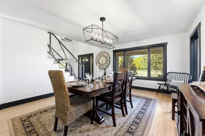 Hardwood-finish flooring, a contemporary open-cage chandelier, black-trimmed windows, a modern cable railing staircase, and a dark-paneled entry door