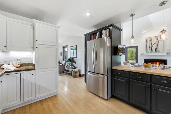 Kitchen featuring stainless steel refrigerator, white cabinetry, dark lower cabinetry, wood-finish flooring, and a fireplace with mantle