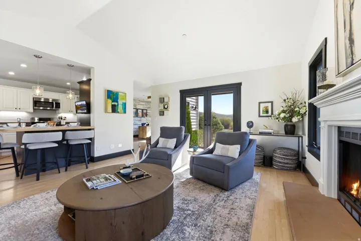 Vaulted ceiling, wood-finish flooring, white fireplace with mantel, French doors, and a kitchen featuring stainless steel appliances
