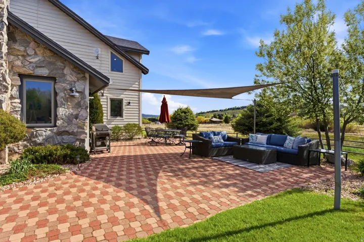Exterior stone facade, tan horizontal siding, and a multi-toned paver patio