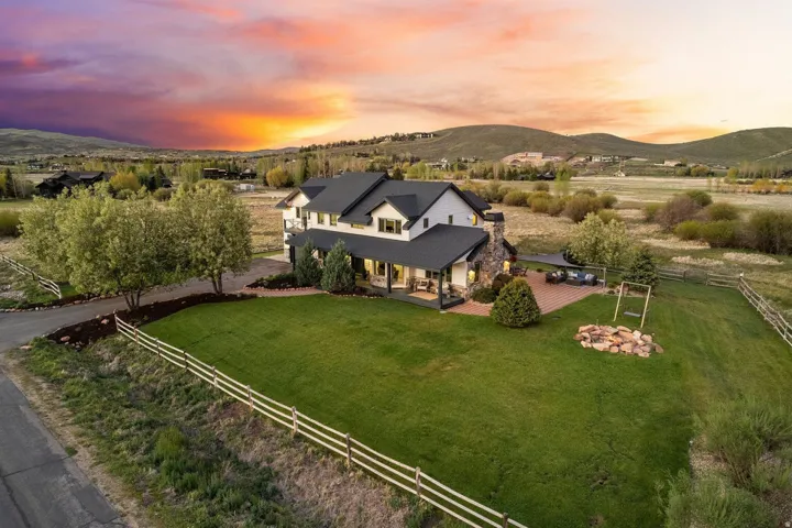 Two-story residence with a black roof, stone chimney, and covered patio