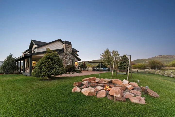 Expansive lawn with a stone fire pit, covered porch, exterior stone chimney, and a gravel patio area