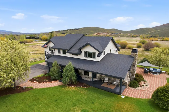 Expansive grounds featuring a manicured lawn, stone-clad chimney, covered porch, and a patterned paver patio