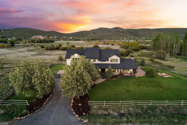 Expansive green lawn with mature trees and a paved driveway leading to the residence, featuring a covered porch