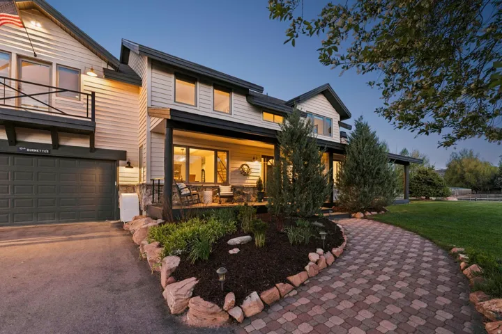 Siding exterior with dark trim accents, covered front porch, integrated garage, upper-level balcony, and a paver pathway