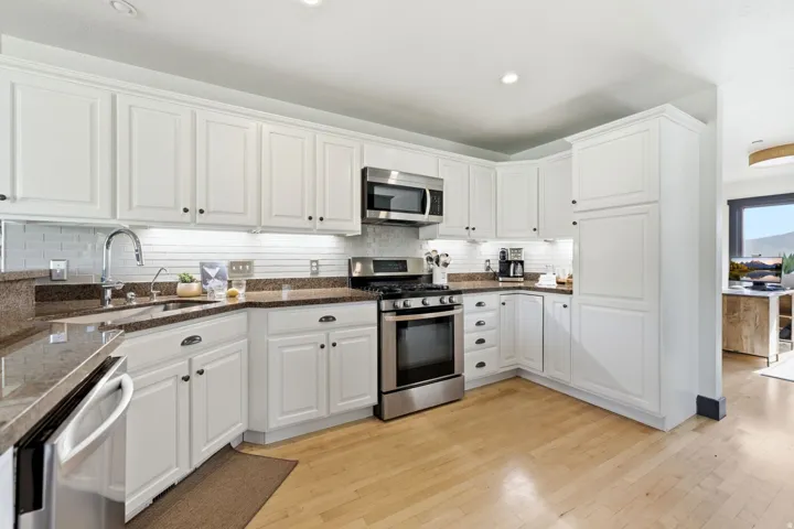 White cabinetry with dark hardware, stainless steel appliances, granite-style countertops, subway tile backsplash, and light wood-finish flooring