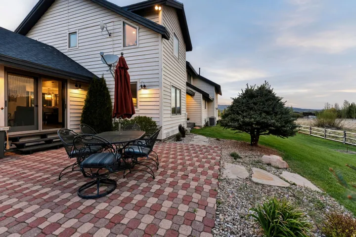 Expansive paver patio with a mature tree, stone landscaping, and a sloped lawn