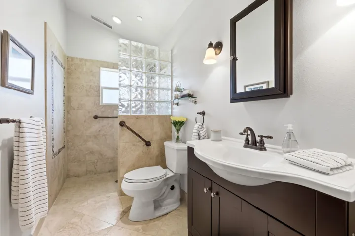 Vanity with a curved white sink and dark wood-finish cabinetry, bronze-finish faucet, and a wall-mounted mirror