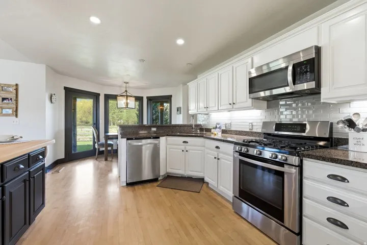 Kitchen featuring wood-finish flooring, white upper and lower cabinetry, stainless steel appliances, dark countertops, and a subway tile backsplash