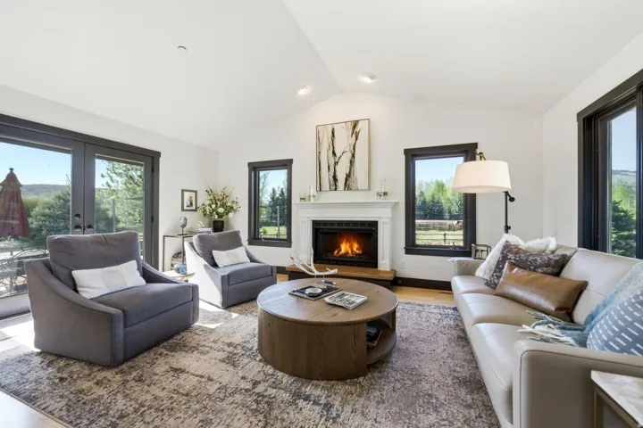 Vaulted ceilings, wood-finish flooring, a white mantel fireplace, and dark-framed windows