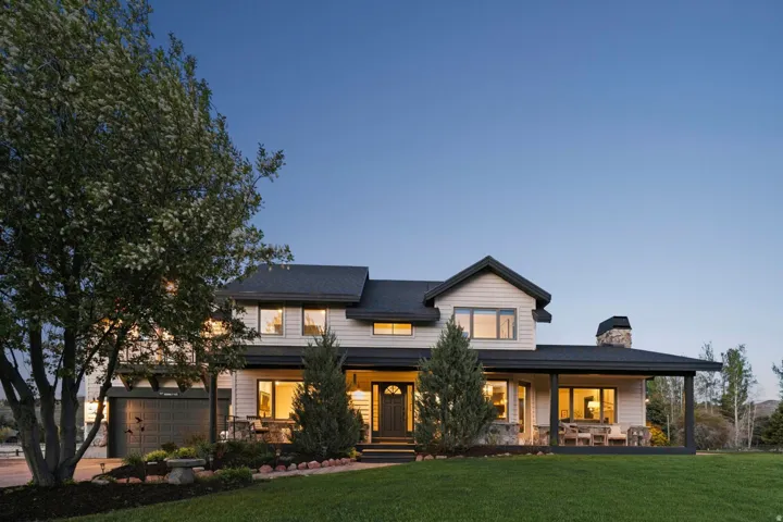 Two-story residence featuring light-colored siding, dark trim, a covered front porch, an integrated garage, and a stone-clad chimney