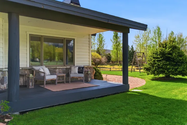 Covered porch with dark wood posts, stone accents, horizontal siding, and a brick pathway