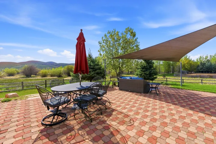Expansive paver patio with a shade sail, bordered by a split-rail fence and mature trees
