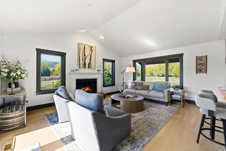 Spacious living area featuring a vaulted ceiling, wood-finish flooring, and a fireplace with a classic mantel