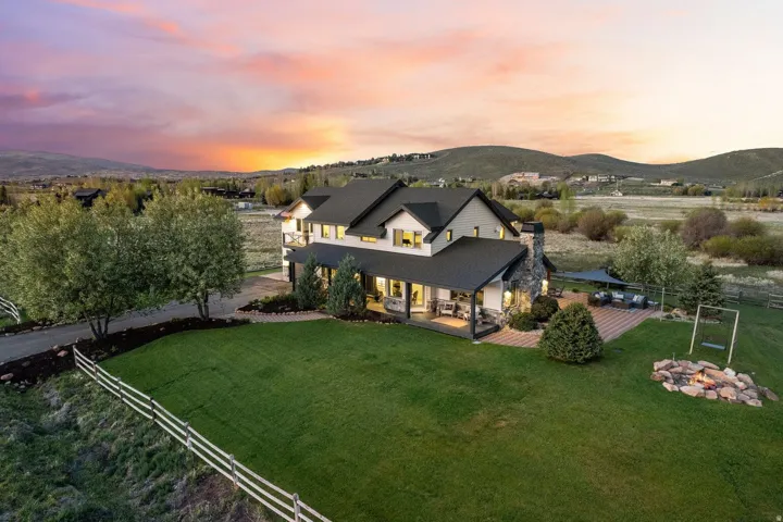 Expansive property featuring a multi-level residence with a covered porch, stone chimney, and an extensive paved patio