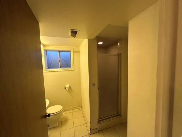Bathroom featuring a window, tile flooring, toilet, and a frosted glass shower enclosure
